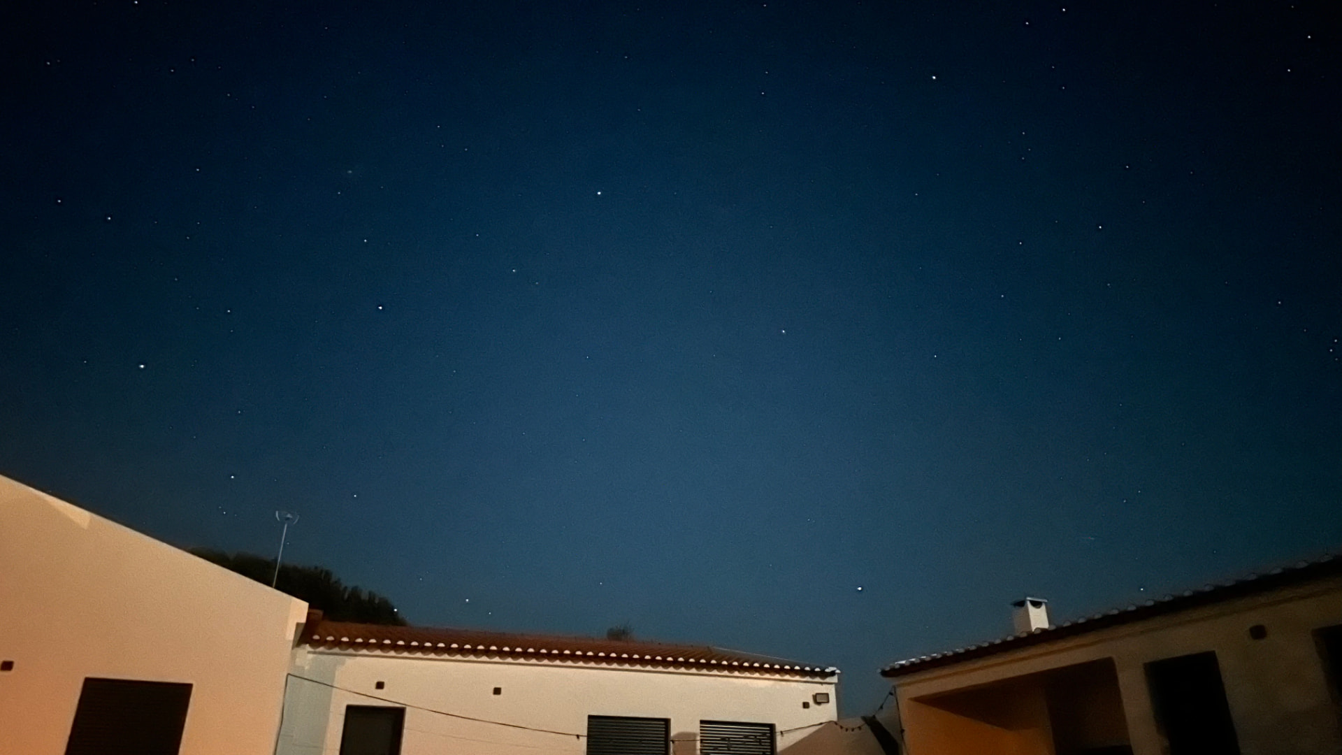 Céu estrelado ao fim da noite visto por cima dos telhados da moradia
