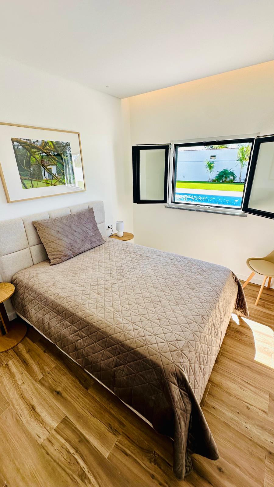 Quarto com cama de casal e janela aberta para a piscina